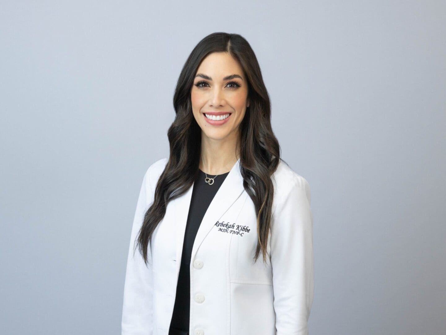 A woman in white lab coat standing next to wall.